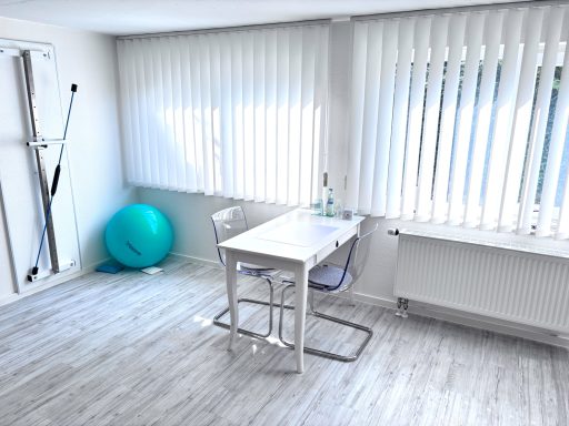 Heller Raum mit Tisch, Stühlen, einer blauen Fitnessball und großen Fenstern.