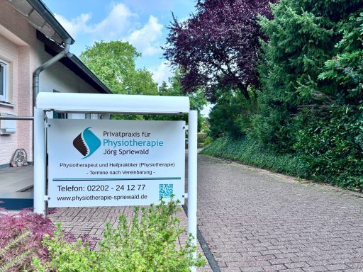 Schild der Physiotherapiepraxis an einem ruhigen Weg, umgeben von Bäumen.