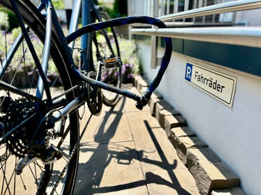Schwarzes Fahrrad mit einem blauen Schloss neben einem Eingangsschild.